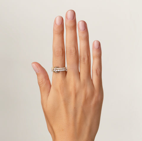 A woman's hand wearing a Spinelli Kilcollin Cadence rind that features a 2.3mm 18k yellow gold bad pave with white diamonds and a 2.8mm 18k white gold band pave with white diamonds, connected by a yellow gold connected pave with diamonds and a white gold connector pave with diamonds. 