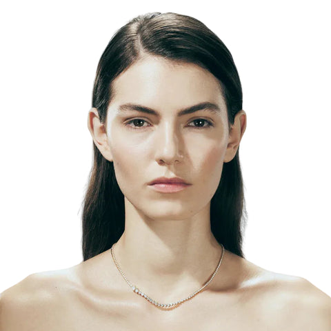 Woman wearing a delicate diamond tennis necklace with graduating size stones against a white background