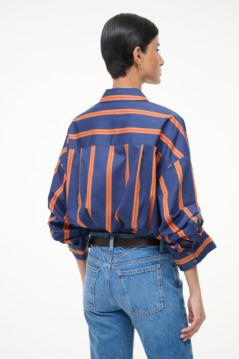 Back-facing woman wearing a blue and orange striped, long sleeve bodysuit with jeans and boots. 