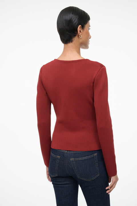 Person wearing a red long-sleeve top and dark jeans on a white background