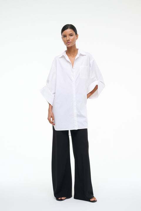 Woman wearing a white shirt dress and black pants on a white background