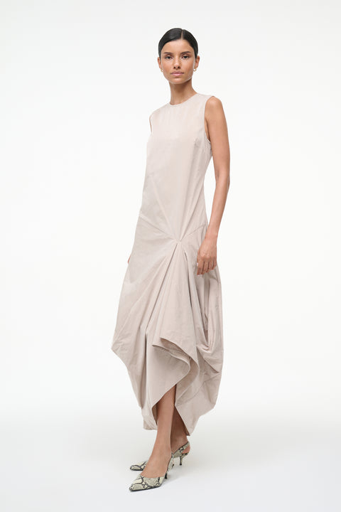 Side-facing woman wearing a beige sleeveless asymmetrical dress 