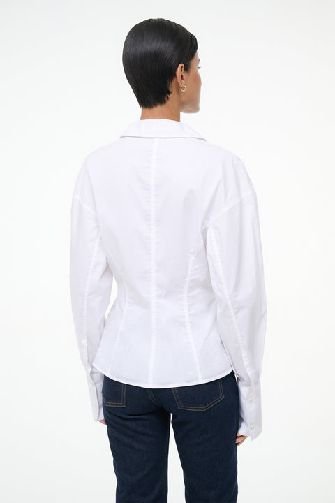 Back-facing Woman wearing a white, long sleeve, button down shirt that features a tailored fit in the waist, paired with jeans.