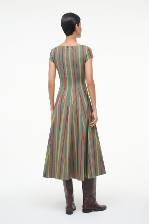 Back-facing woman wearing a green, red, and yellow striped midi dress with cap sleeves with brown boots. 