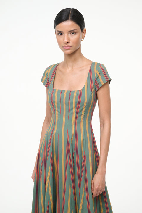 Close up of a woman wearing a green, red, and yellow striped midi dress with cap sleeves and a square neck with brown boots. 