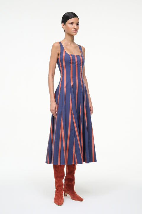Side-facing woman wearing a blue and orange striped sleeveless midi dress with auburn suede boots. 
