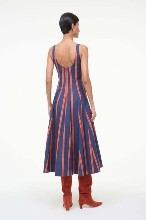 Back-facing woman wearing a blue and orange striped sleeveless midi dress with auburn suede boots. 