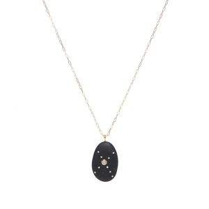 A black oval-shaped stone pendant that features a round diamond in the center of a crisscross pattern of smaller round diamonds, suspended on a gold paperclip chain. 