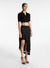 Model turned towards the right in the black asymmetric midi skirt