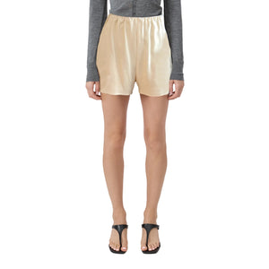 Person wearing beige linen satin shorts on a plain background