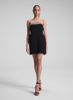 Woman wears black strapless mini dress with crystal embellishment at neckline.