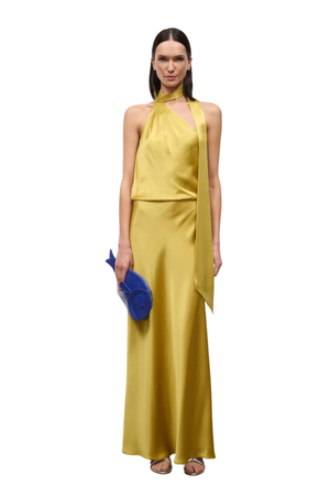 A woman modeling a sleeveless, halter-neck satin dress in a rich yellow color, paired with a matching draped scarf wrap. She is holding a small blue clutch against a solid white background.