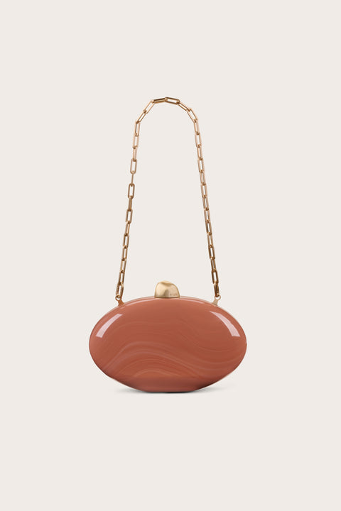 A burnt orange oval-shaped, marbled acrylic clutch that features gold-toned hardware on the top, pictured with the detachable gold chain. 