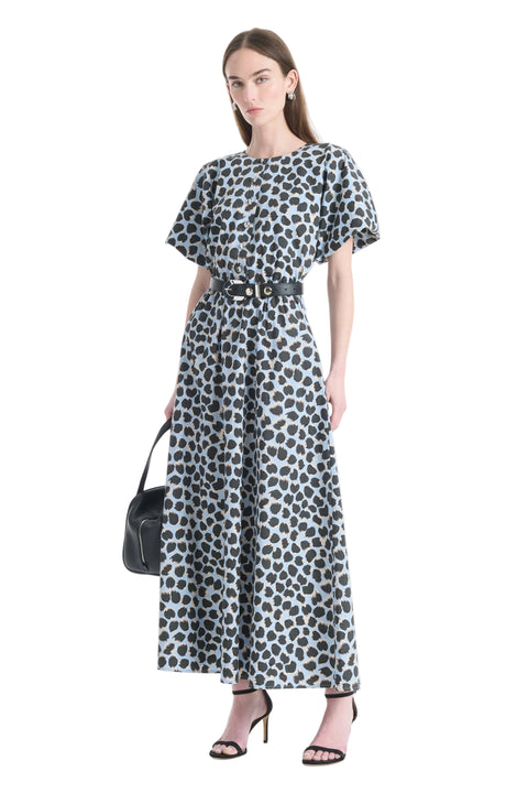 Woman posing wearing a polka dot dress with a belt, holding a black handbag on a white background