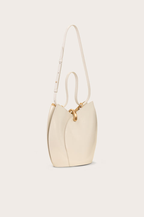 Side view of a white leather shoulder bad that has a curved opening and resembles a tulip, featuring gold hardware and a shoulder and hand strap. 