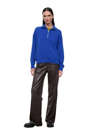 A model stands against a plain white background wearing a bright blue quarter-zip pullover sweater, dark brown wide-leg pants, and black shoes.