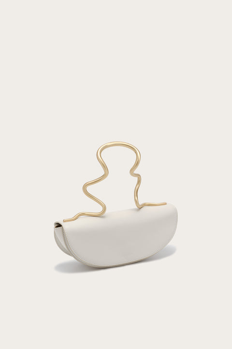Side profile of a white handbag that features a gold-toned, wavy, sculptural top handle.