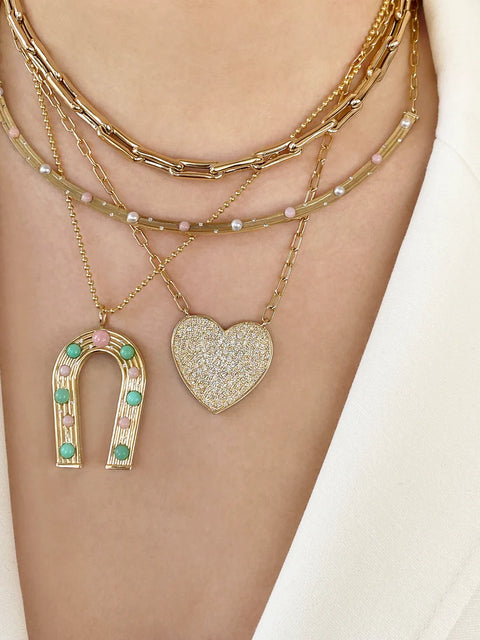 Two gold necklaces with pendants on a person's neck against a neutral background