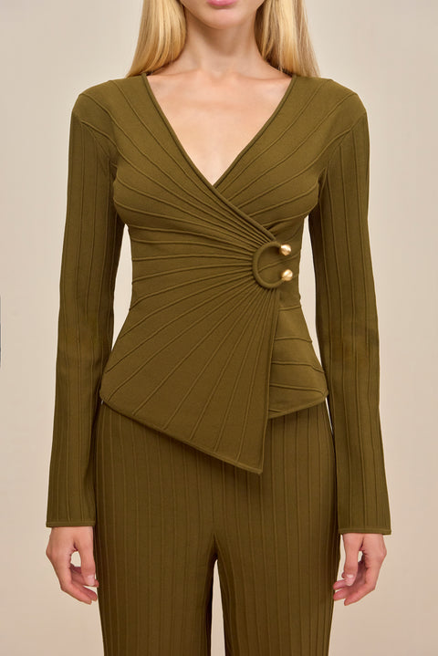 Close up of a woman wearing a green ribbed long sleeve shirt that features a V-neck and a wrap detail secured with gold-toned hardware, styled with matching pants. 