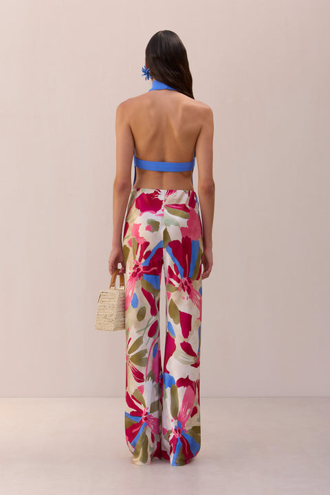 Back view of a woman wearing a periwinkle, knit top that features an open back with a securing strap, paired with floral printed pants. 