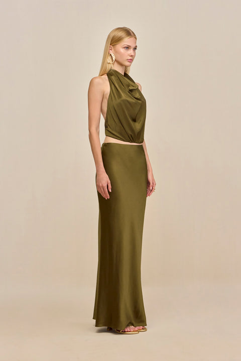 Side-facing woman wearing an olive green silk maxi skirt with a matching halter top. 