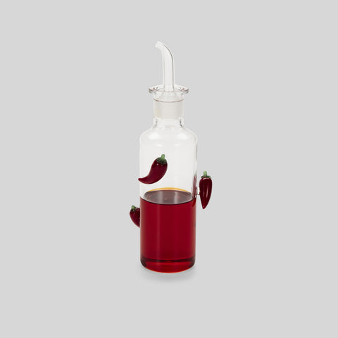 Glass bottle with chilis filled with red liquid.
