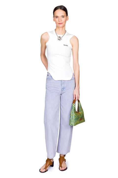 Woman wearing a white sleeveless top and high-rise, light blue jeans, holding a yellow and blue bag on a white background facing front