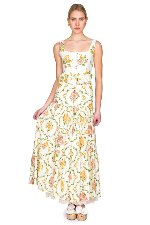 Woman wearing a yellow and pink floral cropped tank and maxi skirt on a white background leaning to the side