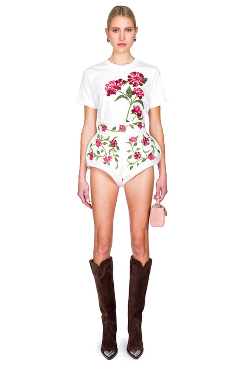 Woman wearing a white floral t-shirt and cropped floral denim mini shorts with brown knee-high boots on a white background front facing