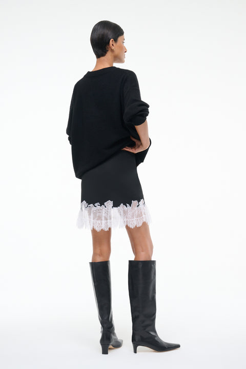 Back-facing woman wearing a black mini skirt with white lace hem, paired with a black sweater and black knee-high boots.