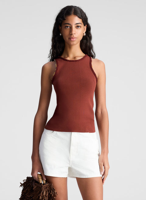 Closer look at woman wearing a rust-colored sleeveless top with beads and white shorts against a plain background