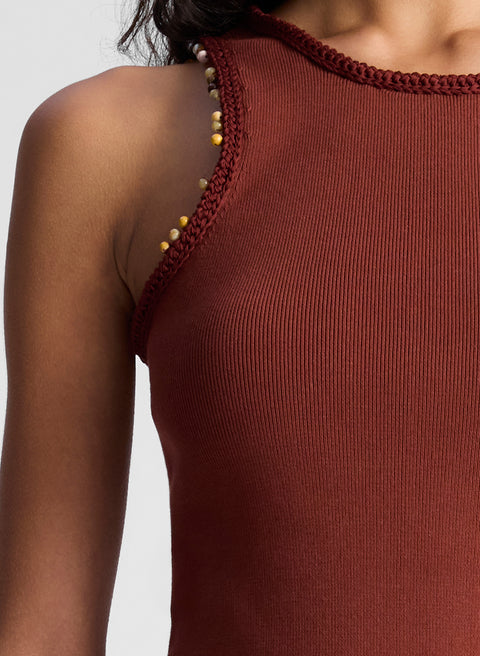 Close of up of woman in Brown sleeveless top with beaded shoulder details on a plain background