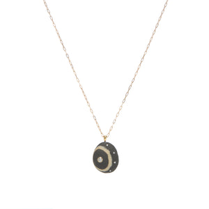 A black stone pendant with a cream wring, accented by one larger diamond and four small diamonds, suspended from a yellow gold paperclip chain. 