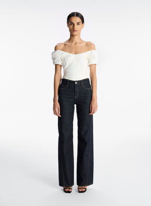 Full body view of a model facing the camera in the white off shoulder crop top