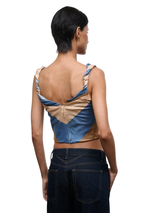 A model shown from the back wearing a color-blocked satin top with blue, beige, and brown panels, paired with dark blue jeans, against a plain white background.