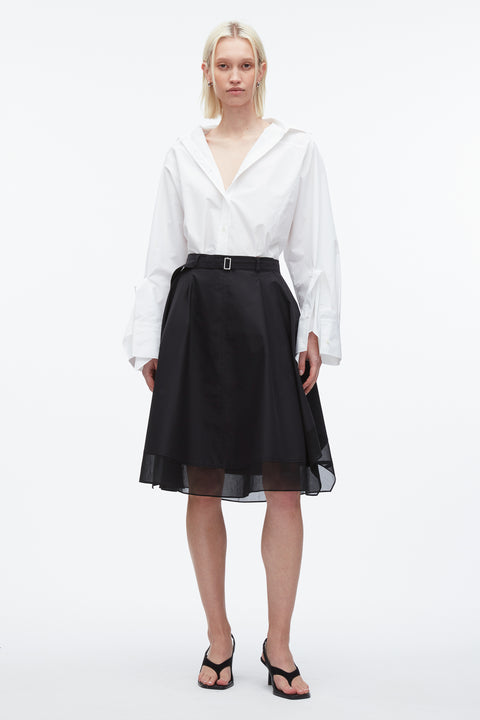 Woman wears black midi skirt with belt featuring organza overlay and white cotton top.