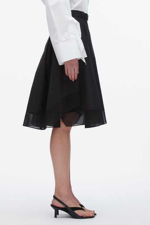 Side view of woman in black midi skirt with chiffon layer and black heels.