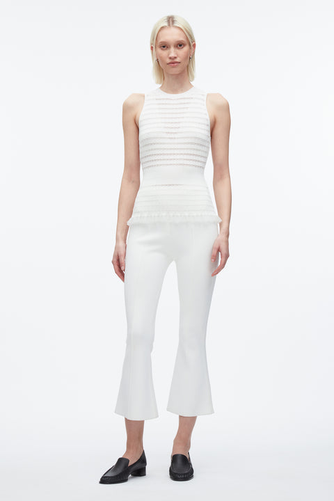 Woman posing in knitted white tank top and white pants and black shoes.