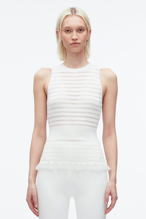 Woman with arms by her side wears white ribbed knit tank top with subtle variegated stripes and ruffled hemline.