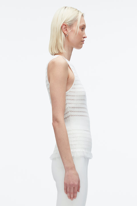 Woman facing the right showing side of white tank top with ruffle hem.