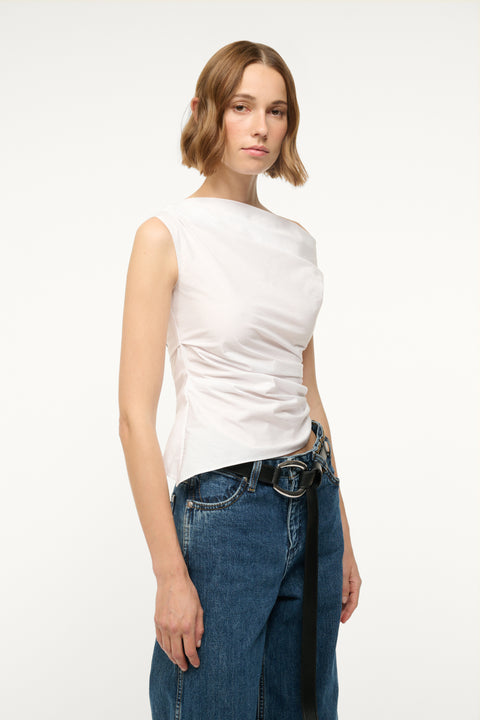 Side-facing woman wearing an asymmetrical white top with ruching throughout the bodice. 