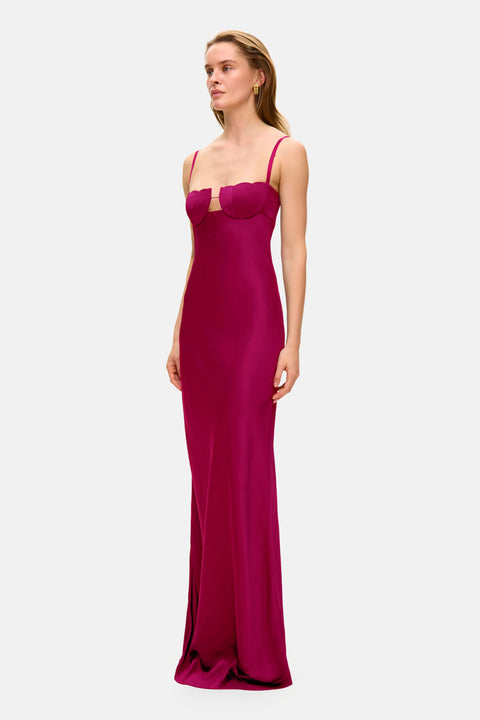 Woman facing the left wearing a magenta thin strap evening gown on a white background