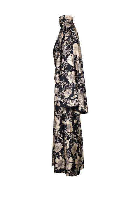 A long-sleeved, high-neck maxi dress with a black base and a beige floral pattern, shown from a side profile view against a plain white background.