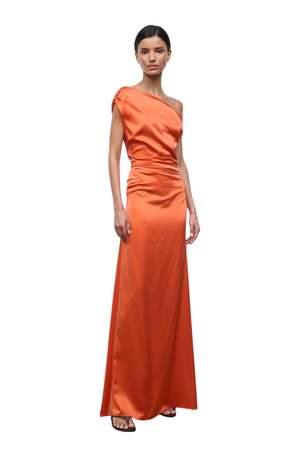 A woman modeling a floor-length, one-shoulder satin gown in a vibrant orange color, standing against a solid white background.