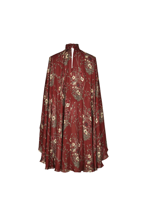 A long-sleeved, high-neck cape-style blouse in a deep burgundy red fabric, decorated with an all-over muted floral and botanical print in beige, olive green, and brown tones, shown against a plain off-white background.