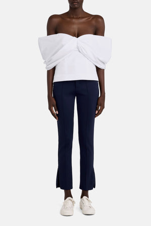 Full body view of a model wearing a white blouse with the navy pants