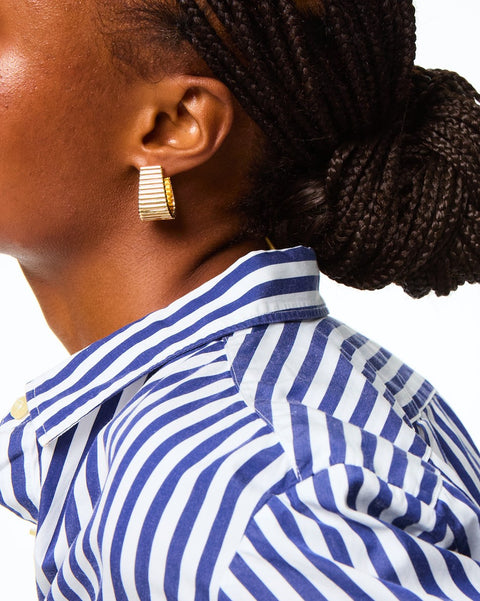 Woman wearing a flat, tapered hoop earring with a ribbed texture. 