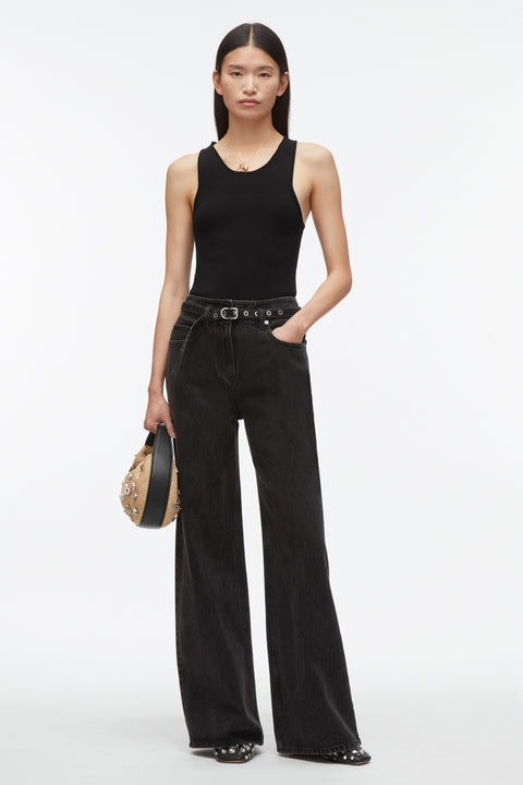 Woman posing in black tank top with black pants and handbag.