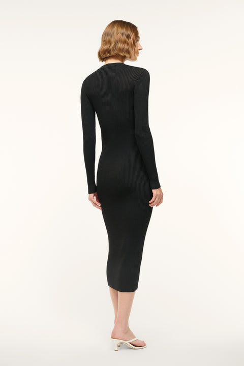 Back view of a woman wearing a black ribbed-knit, long sleeve midi dress, paired with white sandals. 