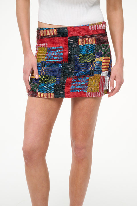 Close up of a woman wearing a beaded mini skirt that features a multicolor patchwork design, paired with a white tank. 